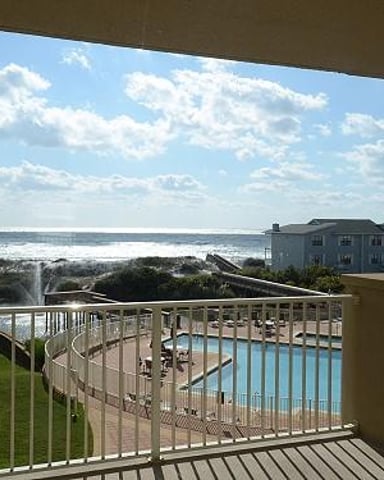 Oceanfront deck with pool, lawn, and beach house view under blue sky
