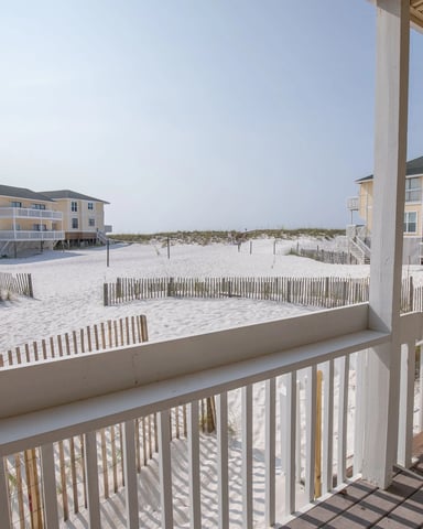 Beachfront deck with white railing overlooking sandy beach, dune fencing, and multi-story vacation rental buildings