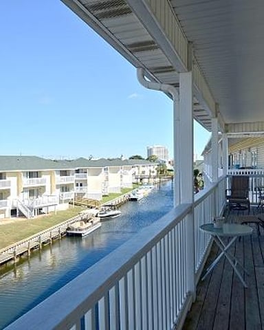 Waterfront deck with railing overlooking canal, neighboring houses, and green lawn on sunny day