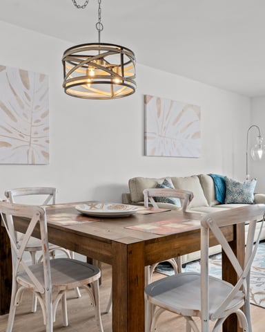 Open-plan dining and living room with wooden table, white chairs, beige sofa, pendant light, and abstract wall art