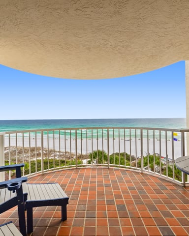 Beachfront balcony with Adirondack chairs, white railing, and view of turquoise ocean and sandy beach