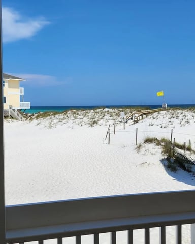 Beachfront view from deck with sand dunes, beach houses, and turquoise ocean under clear blue sky