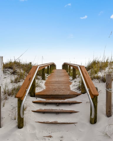 Wooden boardwalk with handrails leading through sand dunes with beach grass under clear blue sky