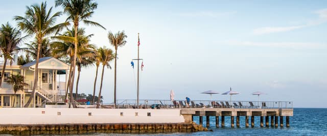 Key West pier with palm trees, lounge chairs, and calm blue water at golden hour