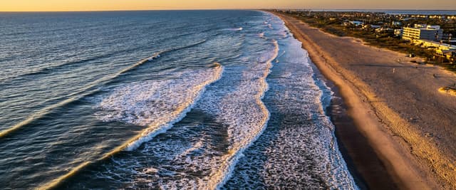Aerial view of Cocoa Beach at sunrise, waves rolling onto white sand with condos along the shoreline
